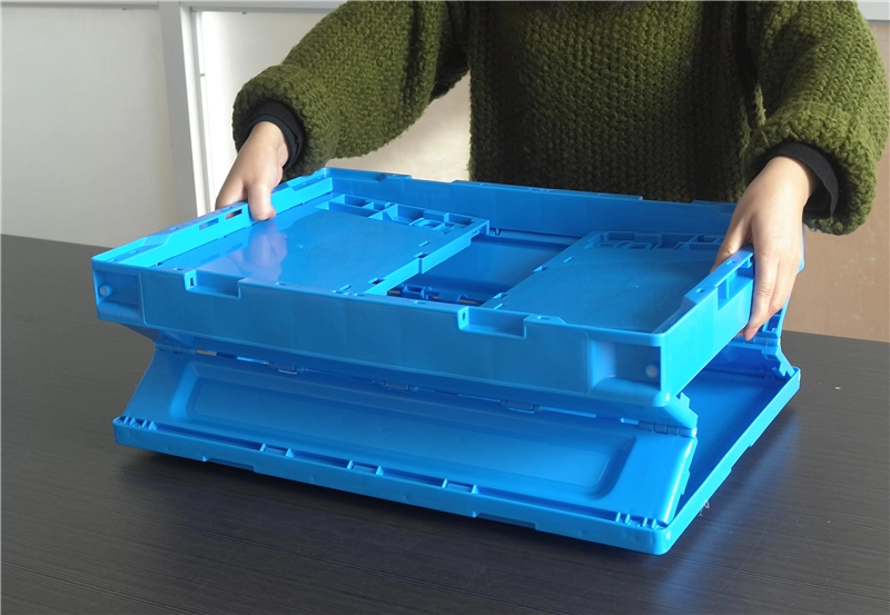 Operator folding a blue collapsible plastic storage crate by hand